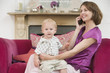 Mother using telephone in living room with baby smiling