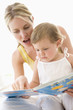 Mother and baby reading book indoors and pointing