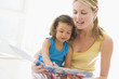 Mother and daughter indoors reading book and smiling