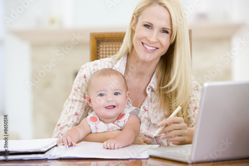 Photo: Mother and baby in dining room with laptop smiling Mother and baby in dining room with laptop smiling