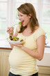Photo: Pregnant woman in kitchen eating a salad smiling Pregnant woman in kitchen eating a salad smiling