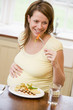 Photo: Pregnant woman in kitchen eating chicken and vegetables smiling Pregnant woman in kitchen eating chicken and vegetables smiling