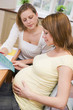 Photo: Pregnant woman in kitchen with friend reading pamphlet Pregnant woman in kitchen with friend reading pamphlet