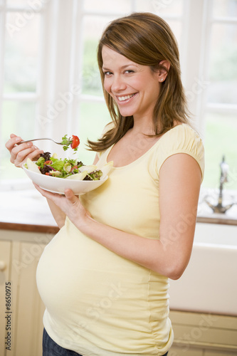 Photo: Pregnant woman in kitchen eating a salad smiling Pregnant woman in kitchen eating a salad smiling