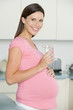 Pregnant woman in kitchen with glass of water smiling