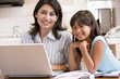Photo: Woman and young girl in kitchen with laptop and paperwork smilin Woman and young girl in kitchen with laptop and paperwork smilin