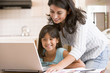 Woman and young girl in kitchen with laptop and paperwork smilin