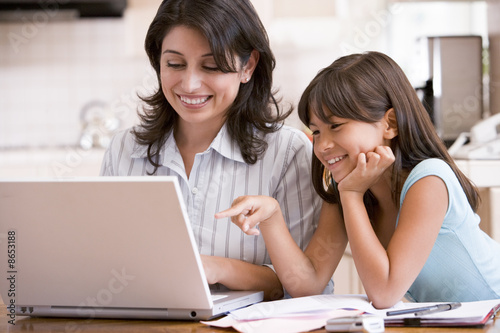 Photo: Woman and young girl in kitchen with laptop and paperwork smilin Woman and young girl in kitchen with laptop and paperwork smilin