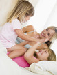 Photo: Woman and two young girls in bed playing and smiling Woman and two young girls in bed playing and smiling