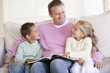 Man and two children sitting in living room reading book and smi