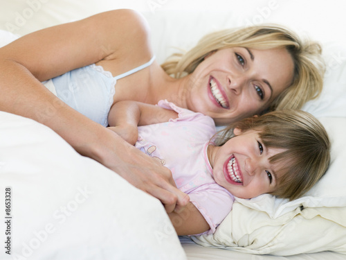 Photo: Woman and young girl in bed smiling Woman and young girl in bed smiling