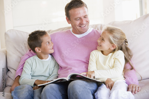 Man and two children sitting in living room reading book and smi Man and two children sitting in living room reading book and smi