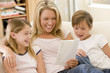 Woman and two young children in living room reading book and smi