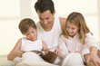 Man with two young children sitting in bed reading a book and sm