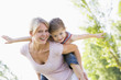 Woman giving young girl piggyback ride outdoors smiling