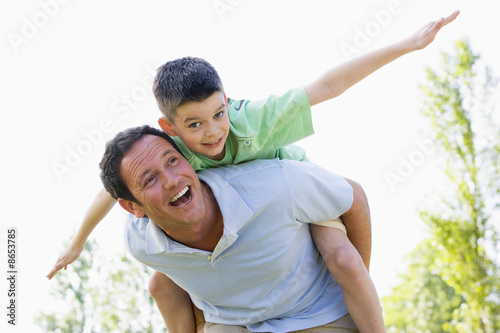 Man giving young boy piggyback ride outdoors smiling