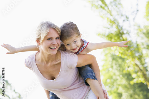 Woman giving young girl piggyback ride outdoors smiling