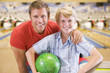 Man and young boy in bowling alley holding ball and smiling
