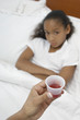 Hand holding medication for girl 7-9 lying in bed