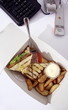 Sandwich in take out carton next to phone on office desk