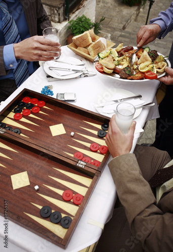 Photo: Closeup of businessmen at taverna with backgammon;appetizers;and ouzo Closeup of businessmen at taverna with backgammon;appetizers;and ouzo