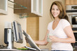Photo: Woman in kitchen at computer with newspaper and coffee smiling Woman in kitchen at computer with newspaper and coffee smiling