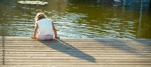 Photo: Daydreaming: little girl sitting on the water chilling her feet Daydreaming: little girl sitting on the water chilling her feet
