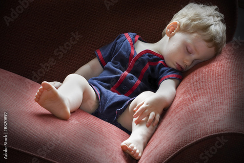 Photo: Young tired boy taking a nap on a red sofa Young tired boy taking a nap on a red sofa
