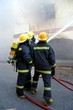 Firemen fighting a fire in a burning building with a water hose Firemen fighting a fire in a burning building with a water hose