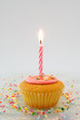 Cupcake with candle on glass plate with candy sprinkles