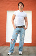 portrait of the young man in blue jeans near red wall portrait of the young man in blue jeans near red wall
