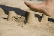 A sand castle at the beach about to be destroyed by a foot A sand castle at the beach about to be destroyed by a foot