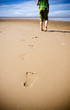 Foto: Young girl walking on the beach leaving footprints in the sand Young girl walking on the beach leaving footprints in the sand