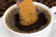 A teaspoon of brown sugar pouring into a cup of black coffee
