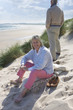 Mature woman sitting on beach, man standing in background