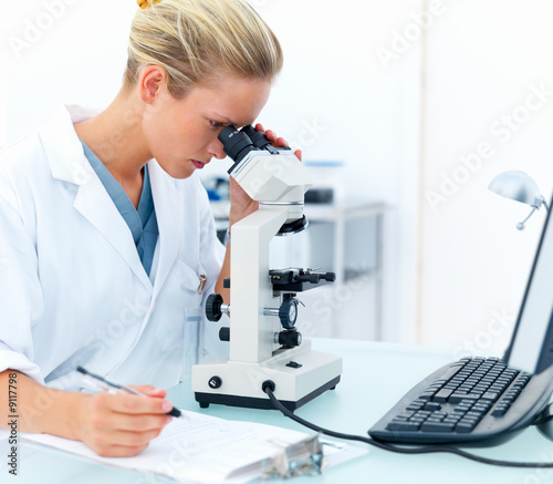 Photo: Young female researcher looking into a microscope Young female researcher looking into a microscope