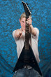 A young guitar player on a blue background pointing