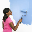 Black woman painting wall blue.