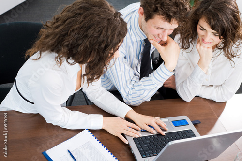 Photo: Happy young business people sitting by table at office Happy young business people sitting by table at office