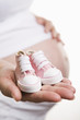 Pregnant woman holding pair of pink shoes for baby girl