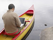 Man sitting in a boat with a laptop.