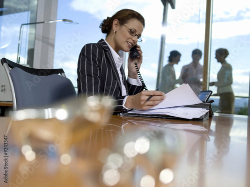Photo: Businesswoman working in office, using telephone, side view Businesswoman working in office, using telephone, side view