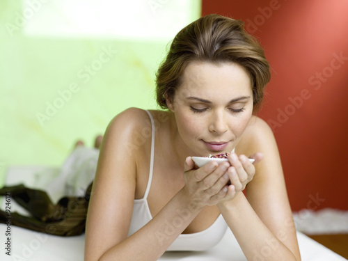 Photo: Woman lying on bed smelling spice in bowl, eyes closed Woman lying on bed smelling spice in bowl, eyes closed