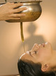 Young woman in spa with oil being poured on forehead, eyes closed