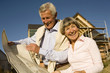 Senior couple holding plan in front of partially built house