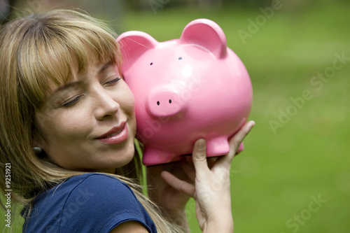 Photo: Beautiful casual woman smiling and holding piggybank - outdoors Beautiful casual woman smiling and holding piggybank - outdoors