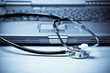 A shot of a stethoscope and a laptop in blue tone