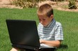 Young boy outdoors on the grass with a laptop computer