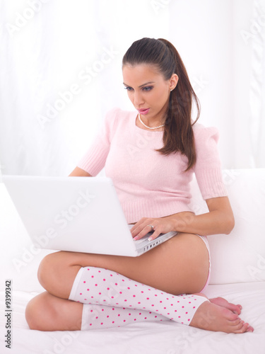 Photo: Young pretty women on white couch relaxing and using laptop Young pretty women on white couch relaxing and using laptop