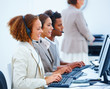 Happy young agents sitting with headsets and using laptop